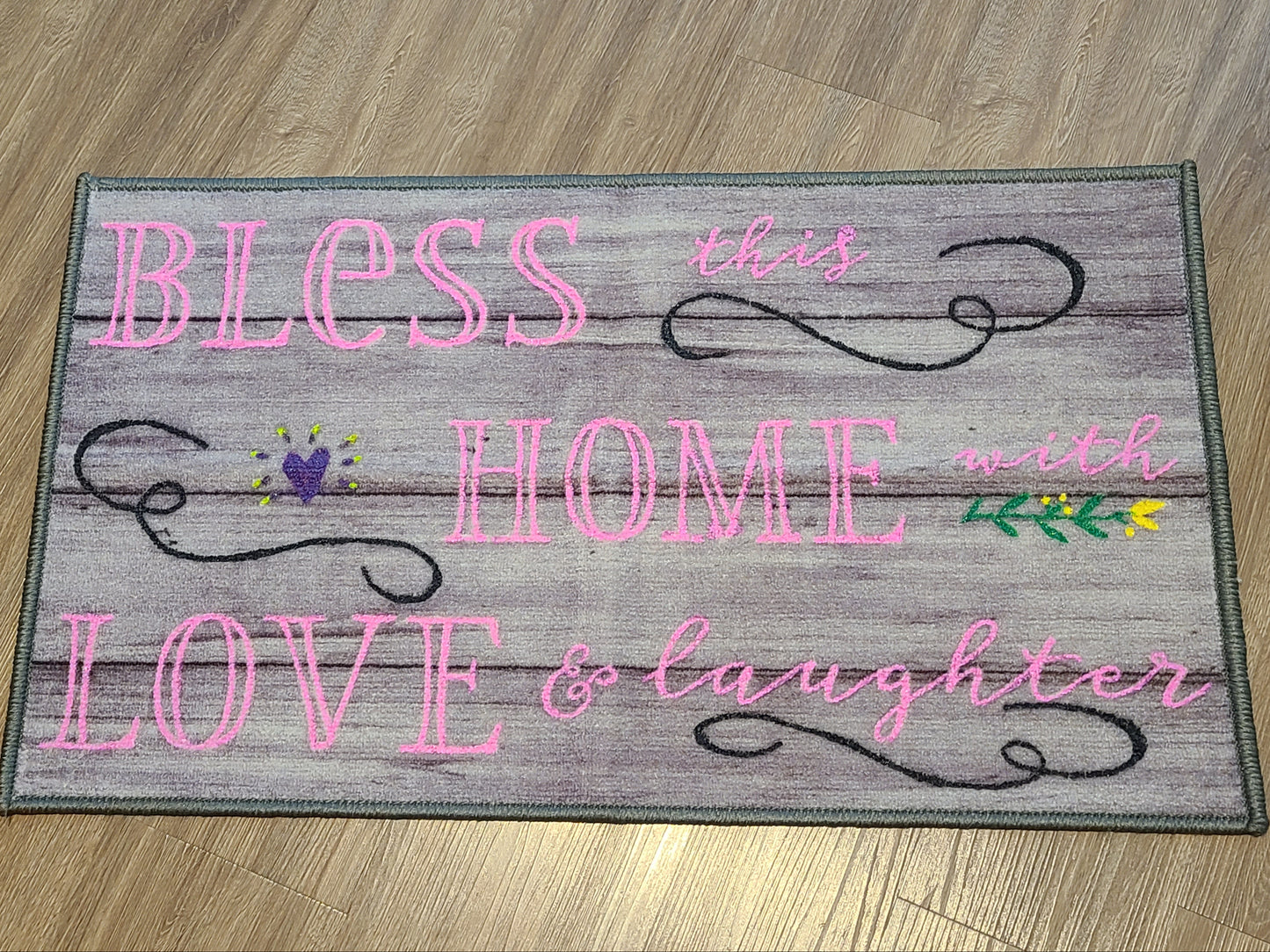 Decorative mat with text 'Bless this home with love & laughter' on a wooden floor.
