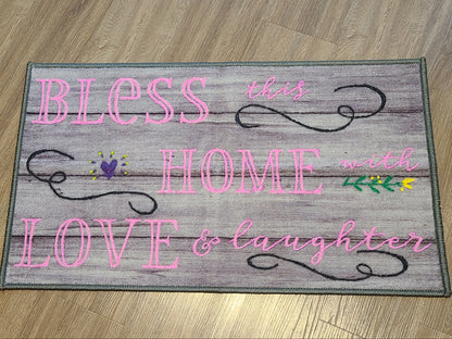 Decorative mat with text 'Bless this home with love & laughter' on a wooden floor.