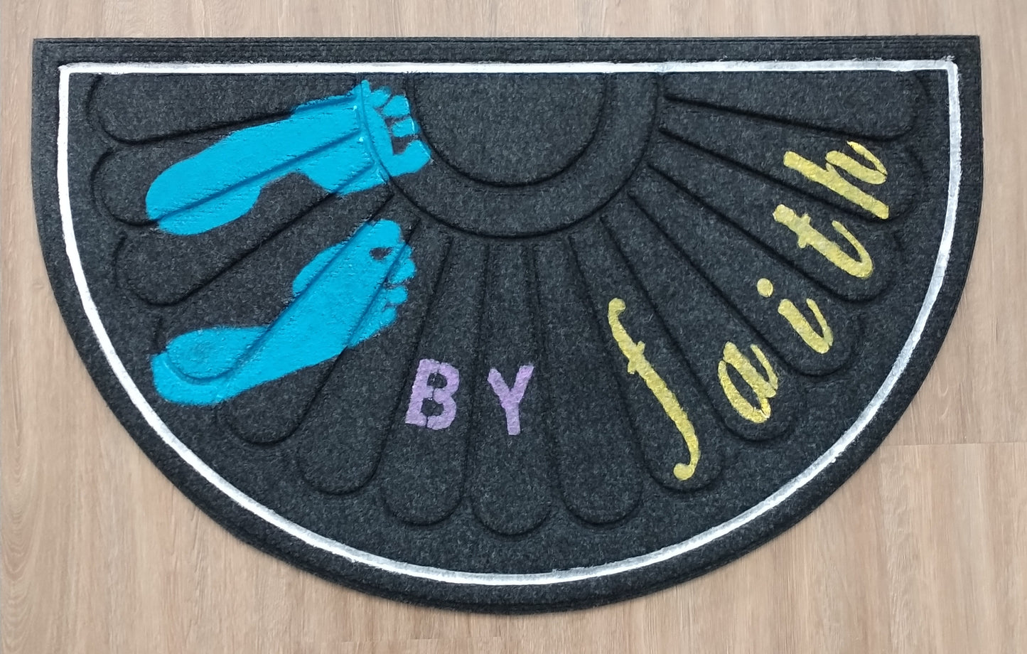 Decorative mat with blue feet, purple 'BY', and yellow 'faith' on a wooden floor.